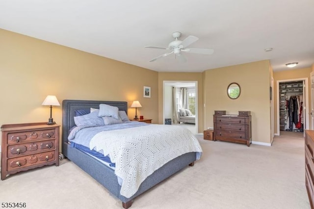 bedroom featuring a walk in closet, ceiling fan, light colored carpet, baseboards, and a closet