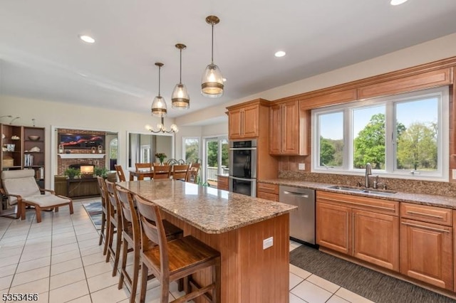 kitchen with a kitchen island, light stone counters, a sink, light tile patterned floors, and stainless steel appliances