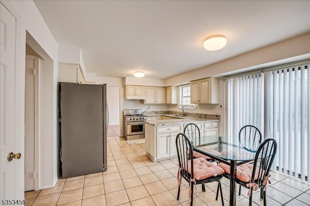 kitchen with cream cabinets, appliances with stainless steel finishes, a sink, light tile patterned floors, and a kitchen island