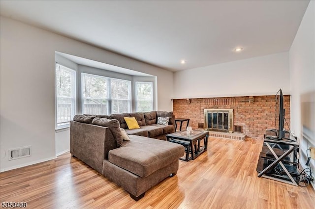 living room featuring visible vents, a brick fireplace, light wood-style floors, and plenty of natural light