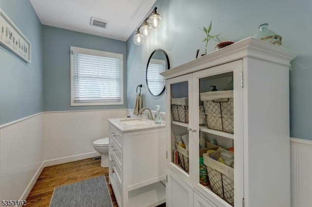 bathroom with visible vents, vanity, wood finished floors, toilet, and a wainscoted wall