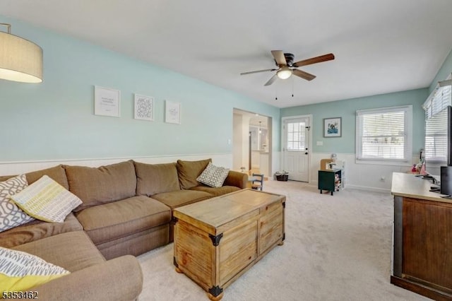 living room with a wainscoted wall, light carpet, and a ceiling fan