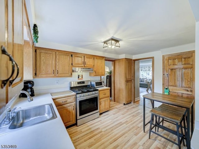 kitchen featuring stainless steel range with gas cooktop, a sink, white microwave, under cabinet range hood, and light countertops