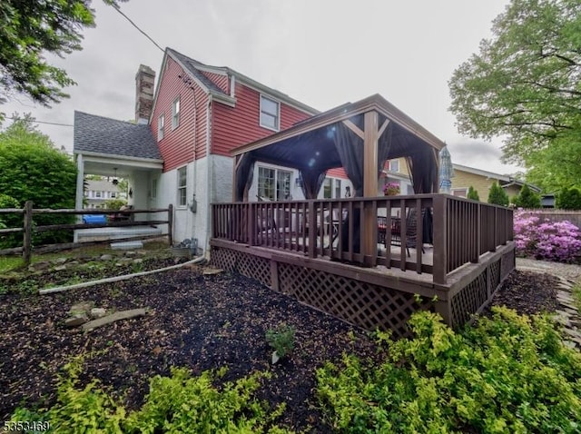 rear view of house featuring a chimney, a wooden deck, and fence