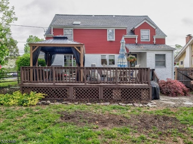 rear view of property with fence, stucco siding, a gazebo, a wooden deck, and roof with shingles