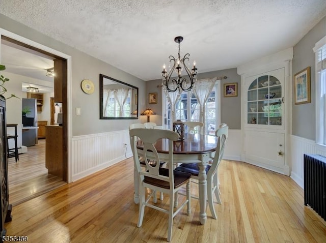 dining space featuring wainscoting, a chandelier, light wood-style flooring, and radiator heating unit