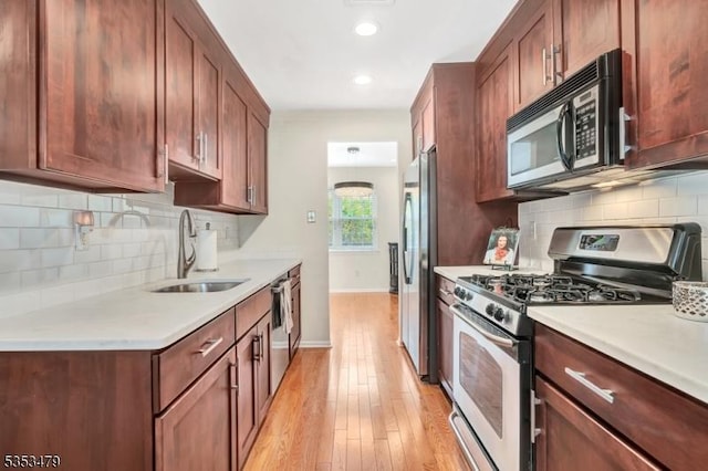 kitchen with a sink, appliances with stainless steel finishes, light wood-style floors, light countertops, and baseboards
