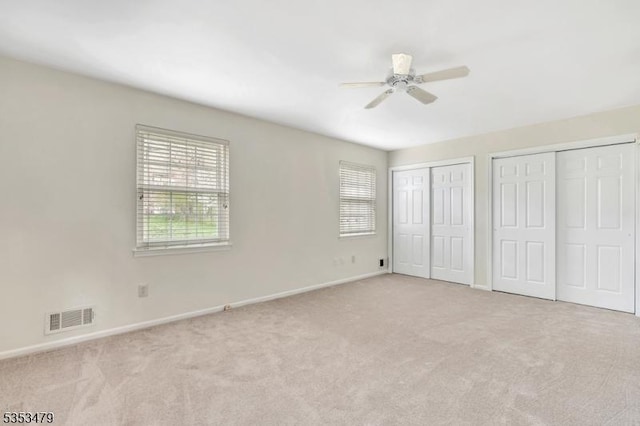 unfurnished bedroom featuring visible vents, multiple closets, carpet flooring, and multiple windows