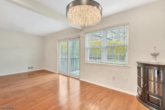 unfurnished dining area featuring visible vents, a notable chandelier, wood finished floors, and baseboards