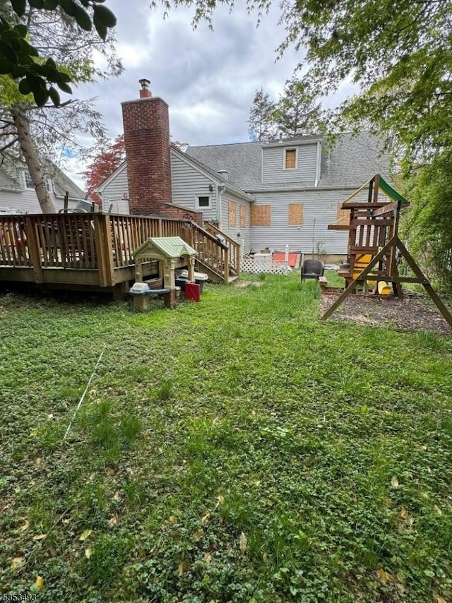 rear view of property featuring a playground, a yard, and a deck