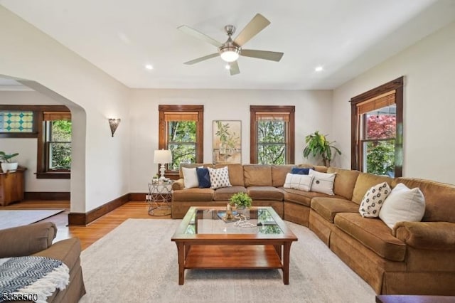 living area with baseboards, plenty of natural light, a ceiling fan, and light wood-type flooring