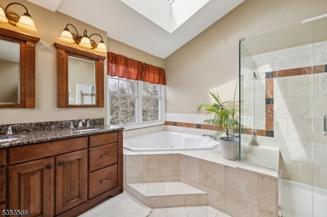 bathroom with double vanity, lofted ceiling with skylight, a garden tub, and a stall shower