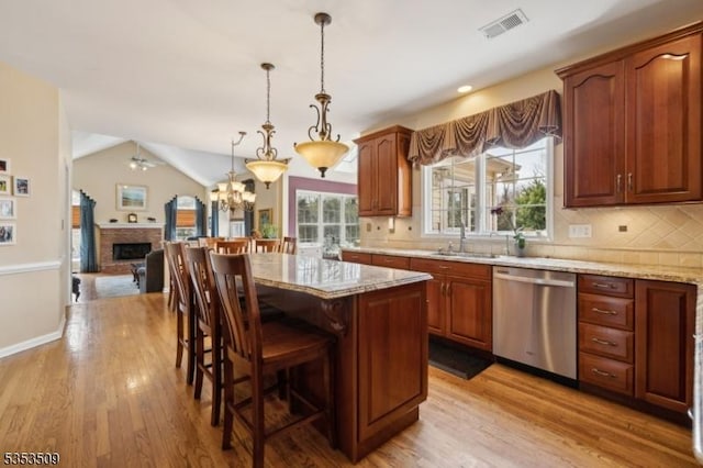 kitchen with stainless steel dishwasher, light stone counters, light wood finished floors, and a sink