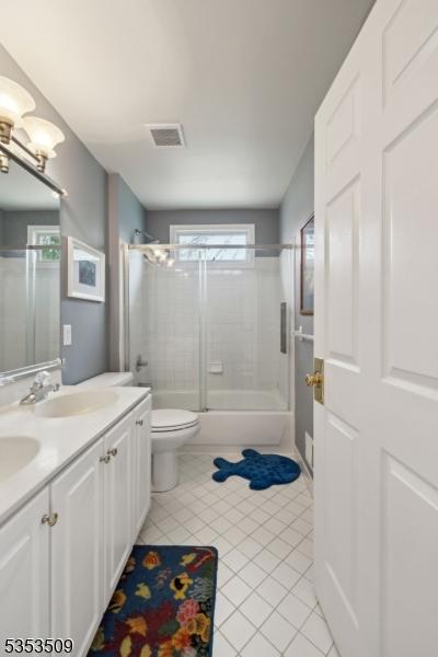 bathroom featuring shower / bath combination with glass door, a sink, visible vents, toilet, and tile patterned floors