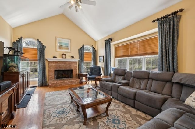 living room featuring hardwood / wood-style floors, high vaulted ceiling, a ceiling fan, and a fireplace