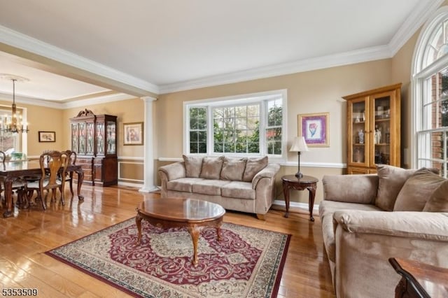 living room featuring ornamental molding, a notable chandelier, light wood-style flooring, and ornate columns