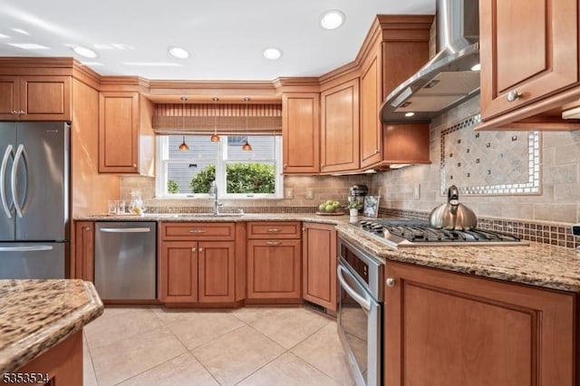 kitchen featuring brown cabinetry, a sink, wall chimney range hood, and stainless steel appliances