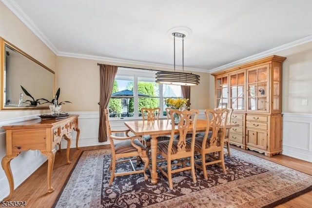 dining space featuring ornamental molding, light wood finished floors, a decorative wall, and a wainscoted wall