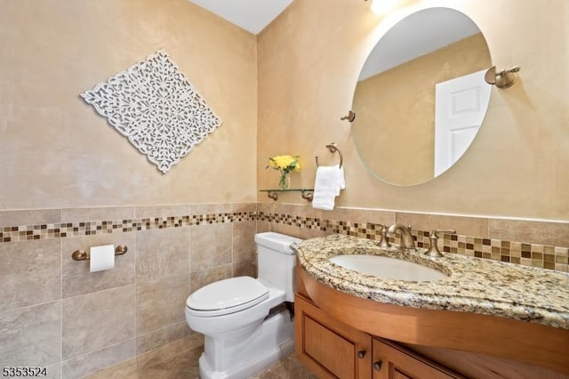 half bath with tile walls, vanity, and toilet