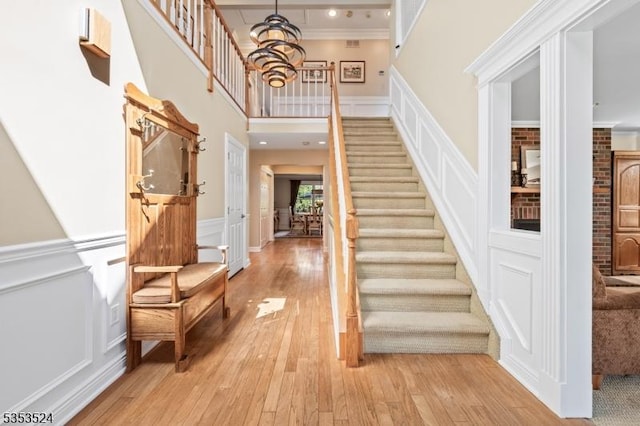 foyer entrance with crown molding, a wainscoted wall, light wood finished floors, a decorative wall, and stairs