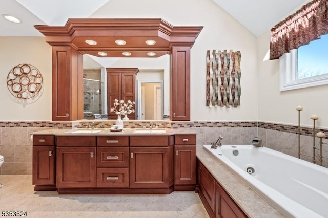 full bath with double vanity, tile walls, a sink, a stall shower, and vaulted ceiling