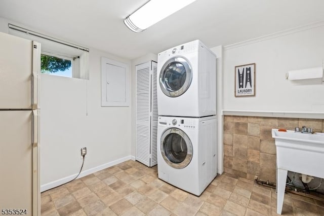 laundry area featuring stone finish floor, laundry area, stacked washer and dryer, and tile walls