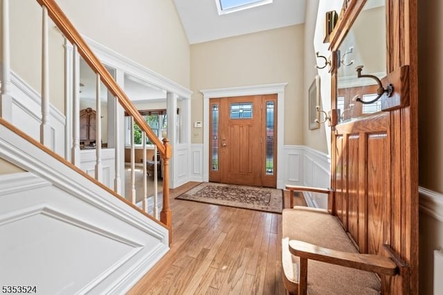 entryway with wainscoting, a decorative wall, light wood-style floors, a high ceiling, and stairway