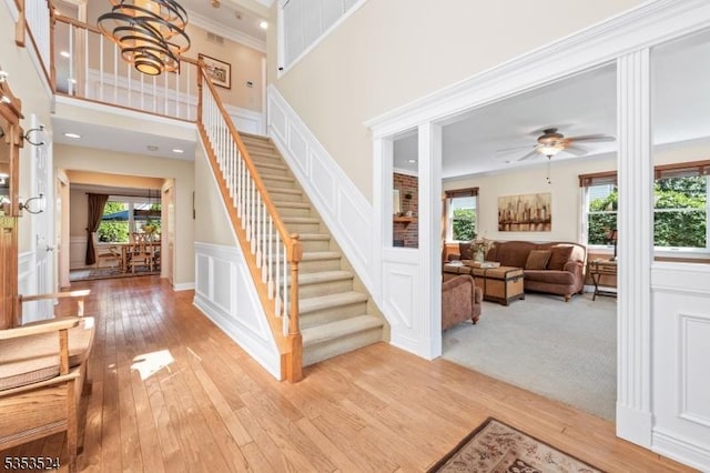 stairs featuring crown molding, wainscoting, a decorative wall, a ceiling fan, and hardwood / wood-style flooring