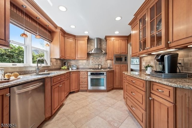 kitchen with wall chimney range hood, brown cabinetry, backsplash, appliances with stainless steel finishes, and a sink