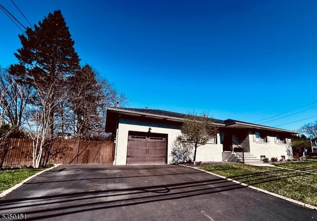 ranch-style home with brick siding, fence, aphalt driveway, a front yard, and an attached garage