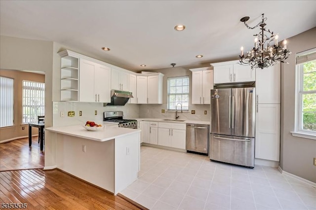 kitchen with open shelves, a sink, a chandelier, stainless steel appliances, and a peninsula