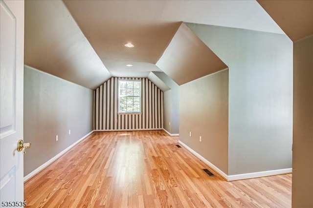 additional living space featuring baseboards, visible vents, wood finished floors, and vaulted ceiling