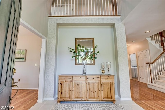 entrance foyer with light wood-style floors, stairs, baseboards, and washer / dryer