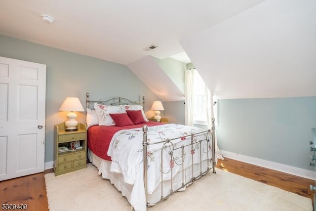 bedroom featuring lofted ceiling, visible vents, light wood finished floors, and baseboards
