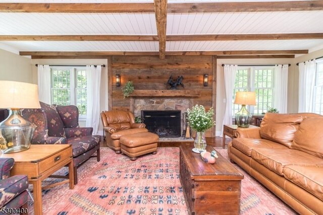 living room featuring beamed ceiling, a stone fireplace, wood finished floors, and wood ceiling