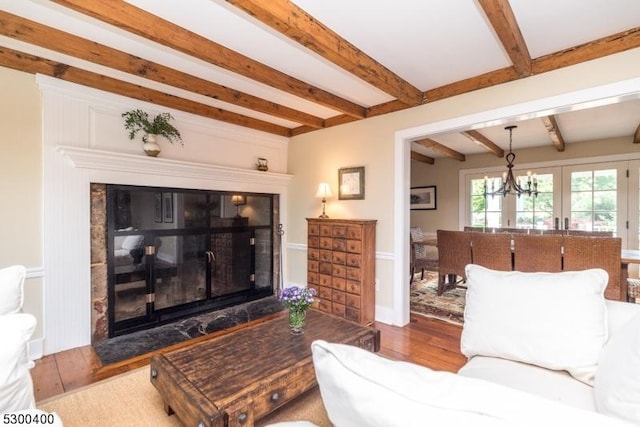 living room with beam ceiling, a glass covered fireplace, wood finished floors, and a notable chandelier