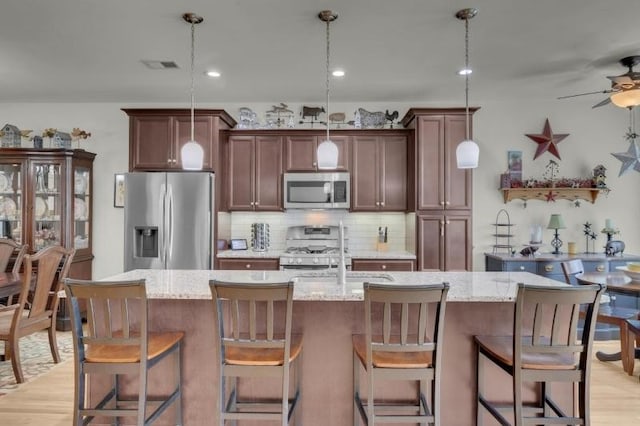 kitchen featuring light stone counters, an island with sink, stainless steel appliances, backsplash, and visible vents