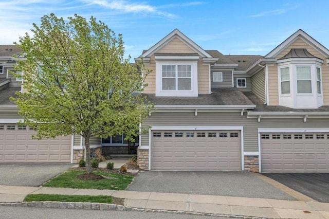 view of property featuring a garage, a shingled roof, driveway, and stone siding