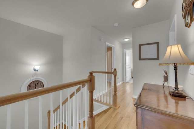 hall featuring baseboards, light wood-type flooring, and an upstairs landing