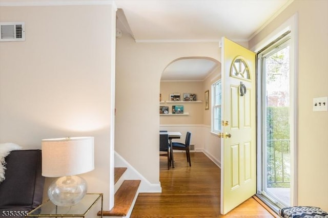foyer with visible vents, wood finished floors, arched walkways, and crown molding