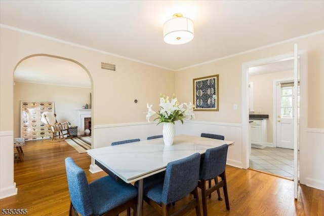 dining room featuring crown molding, visible vents, light wood-style floors, arched walkways, and a brick fireplace