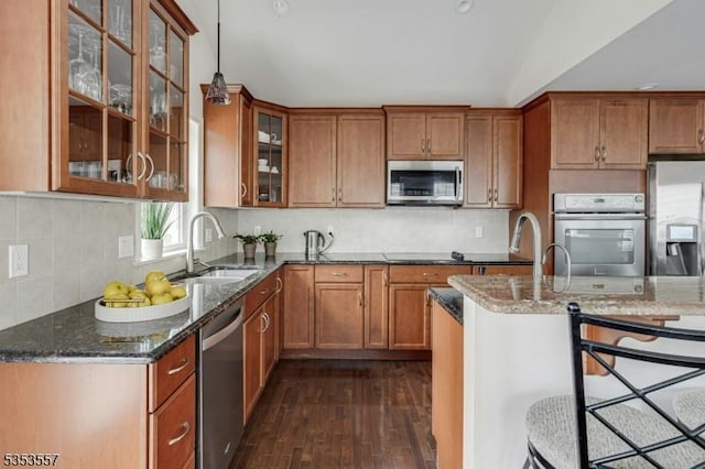 kitchen featuring brown cabinets, a sink, dark stone countertops, dark wood-style floors, and stainless steel appliances