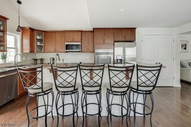 kitchen featuring brown cabinetry, dark wood-style flooring, a kitchen bar, a sink, and stainless steel appliances