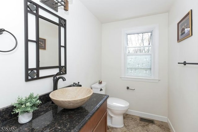 half bathroom with vanity, baseboards, toilet, and visible vents