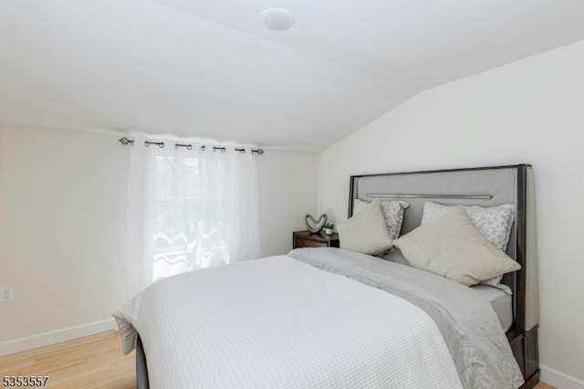 bedroom featuring baseboards, light wood-type flooring, and lofted ceiling