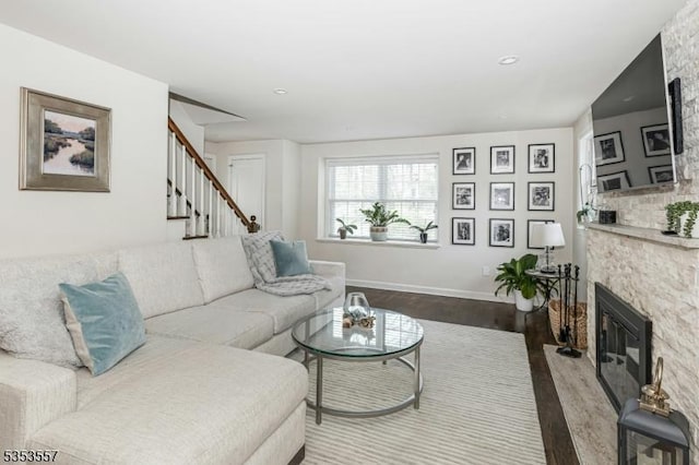 living area featuring a stone fireplace, baseboards, stairs, and wood finished floors
