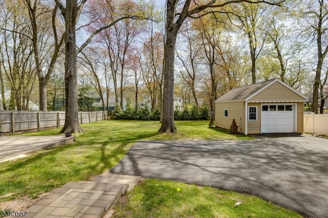 view of yard with fence, an outdoor structure, aphalt driveway, and a garage