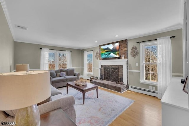 living room featuring a baseboard radiator, light wood-style floors, a brick fireplace, visible vents, and crown molding