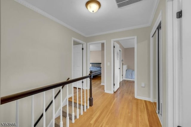 hall with visible vents, light wood-type flooring, ornamental molding, and baseboards