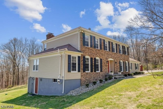 view of side of property featuring a chimney, a yard, and brick siding